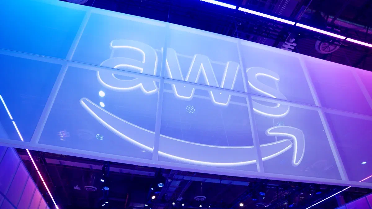 An illuminated AWS sign above the floor of the re:Invent expo hall, lit in blue and violet